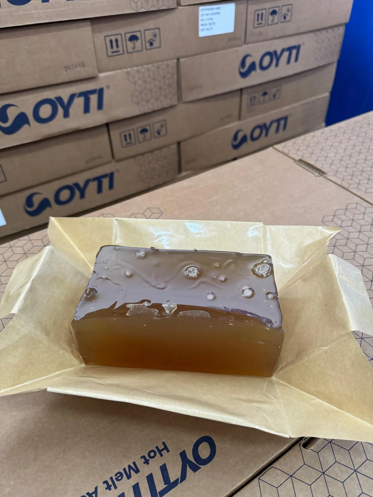 Amber hotmelt adhesive block on release paper with OYTI cartons in the background