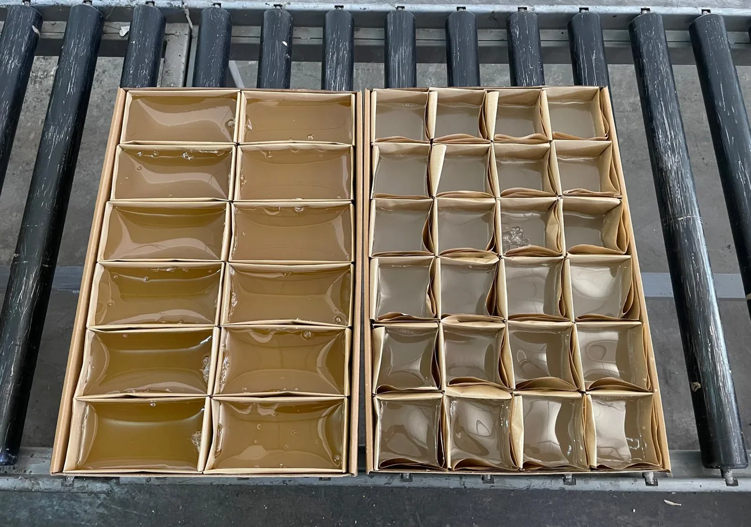 Two cartons containing adhesive blocks in individual lined compartments on a roller conveyor